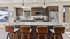Una cocina moderna con una isla grande, armarios de madera, electrodomésticos de acero inoxidable e iluminación colgante.