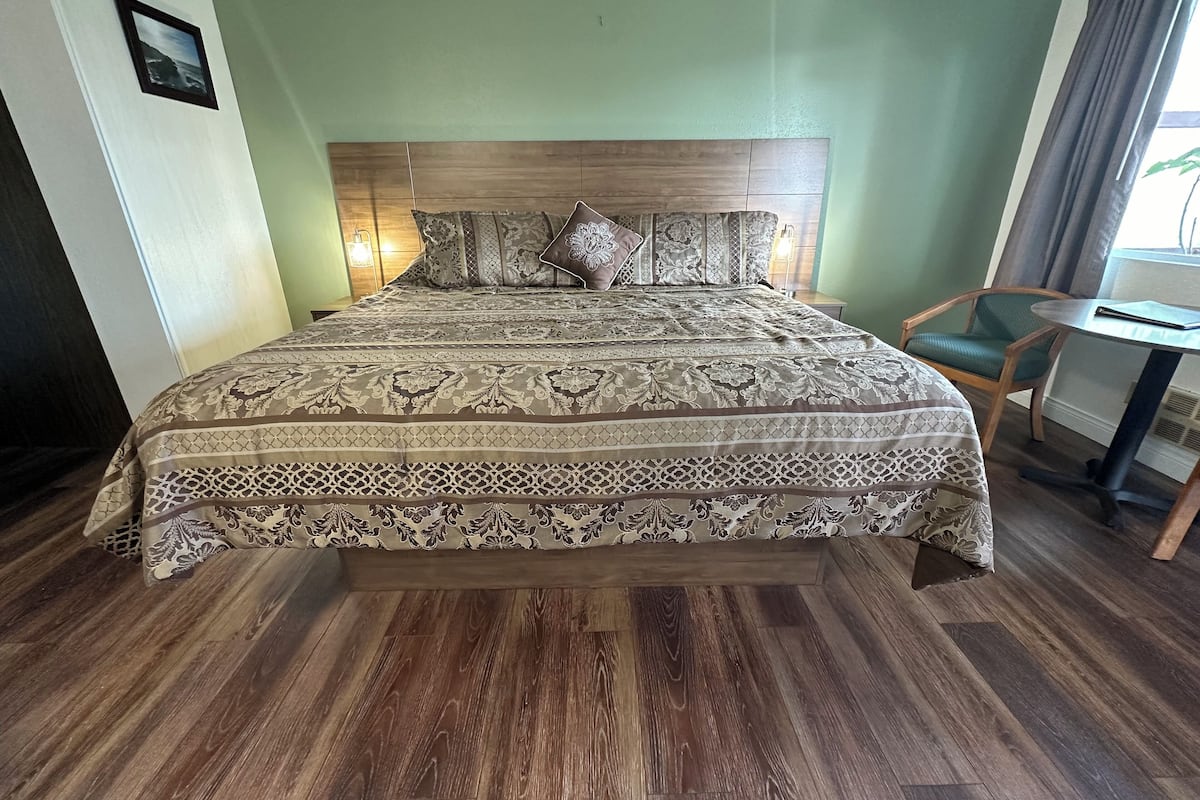 A neatly made bed with a patterned bedspread, a wooden headboard, and a green chair beside a small table.