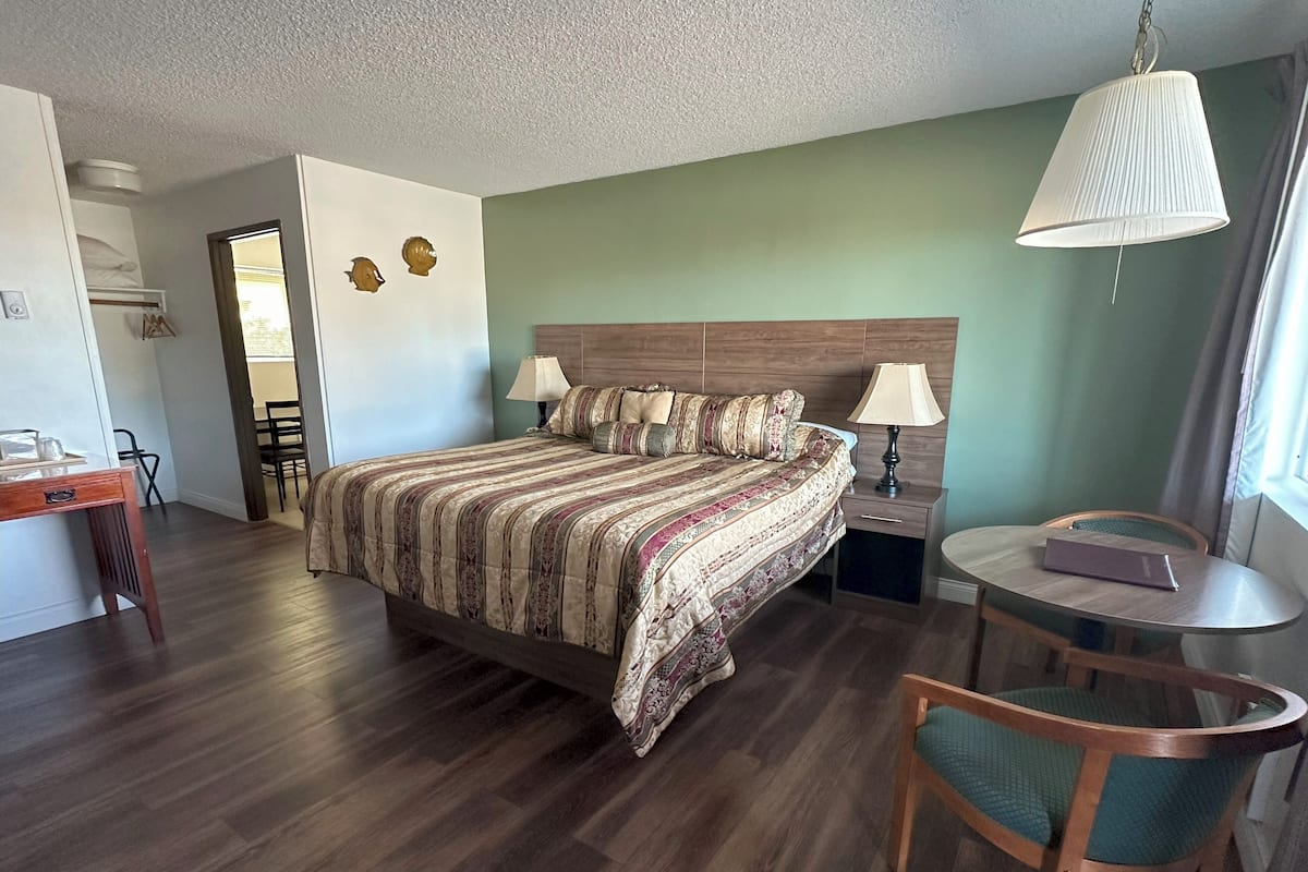 A bedroom with a wooden bed, two bedside tables with lamps, a round table with a chair, and a view of the hallway.