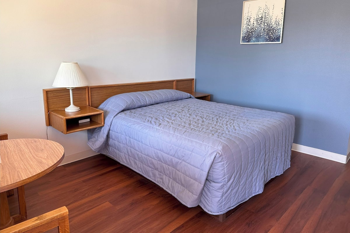 A neatly arranged bedroom with a bed, bedside table, lamp, and a small wooden table.