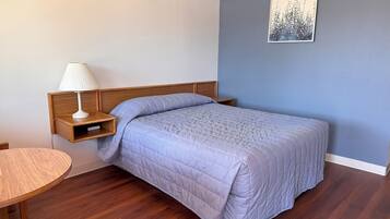 A neatly arranged bedroom with a bed, bedside table, lamp, and a small wooden table.