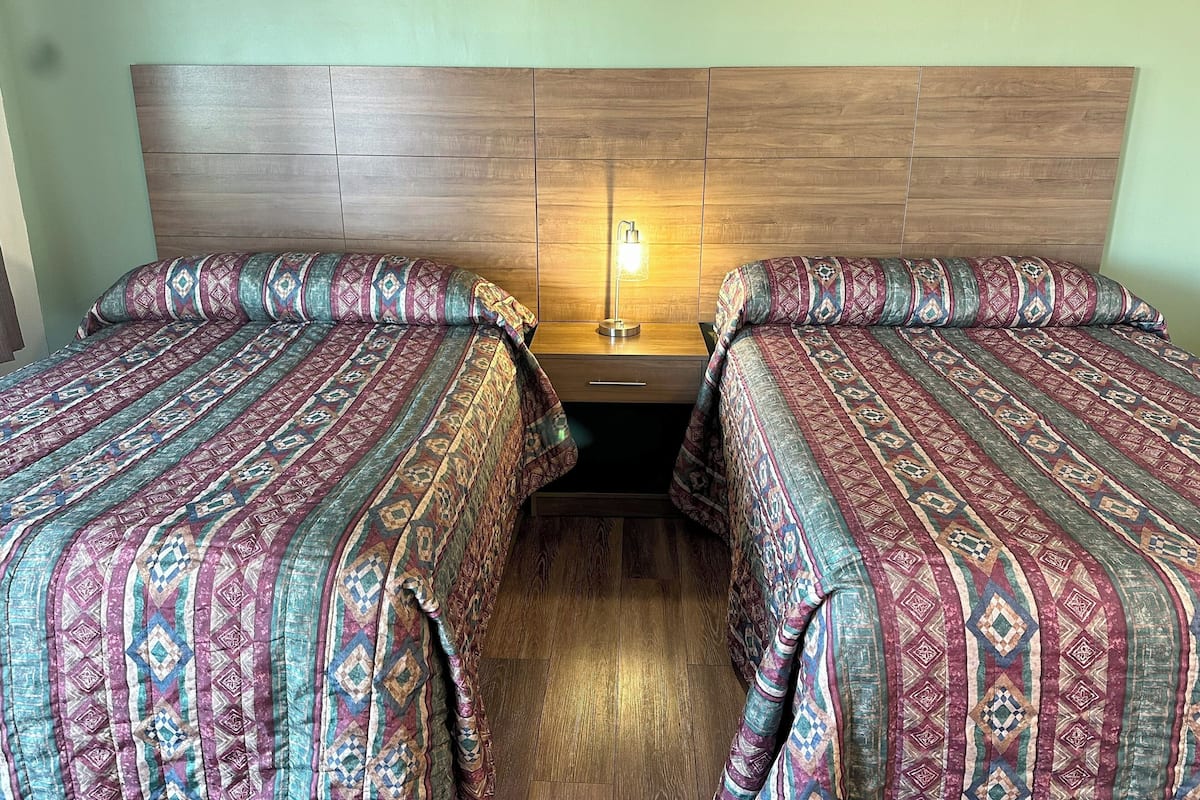 A double bed with patterned bedding, a wooden headboard, and a bedside lamp.
