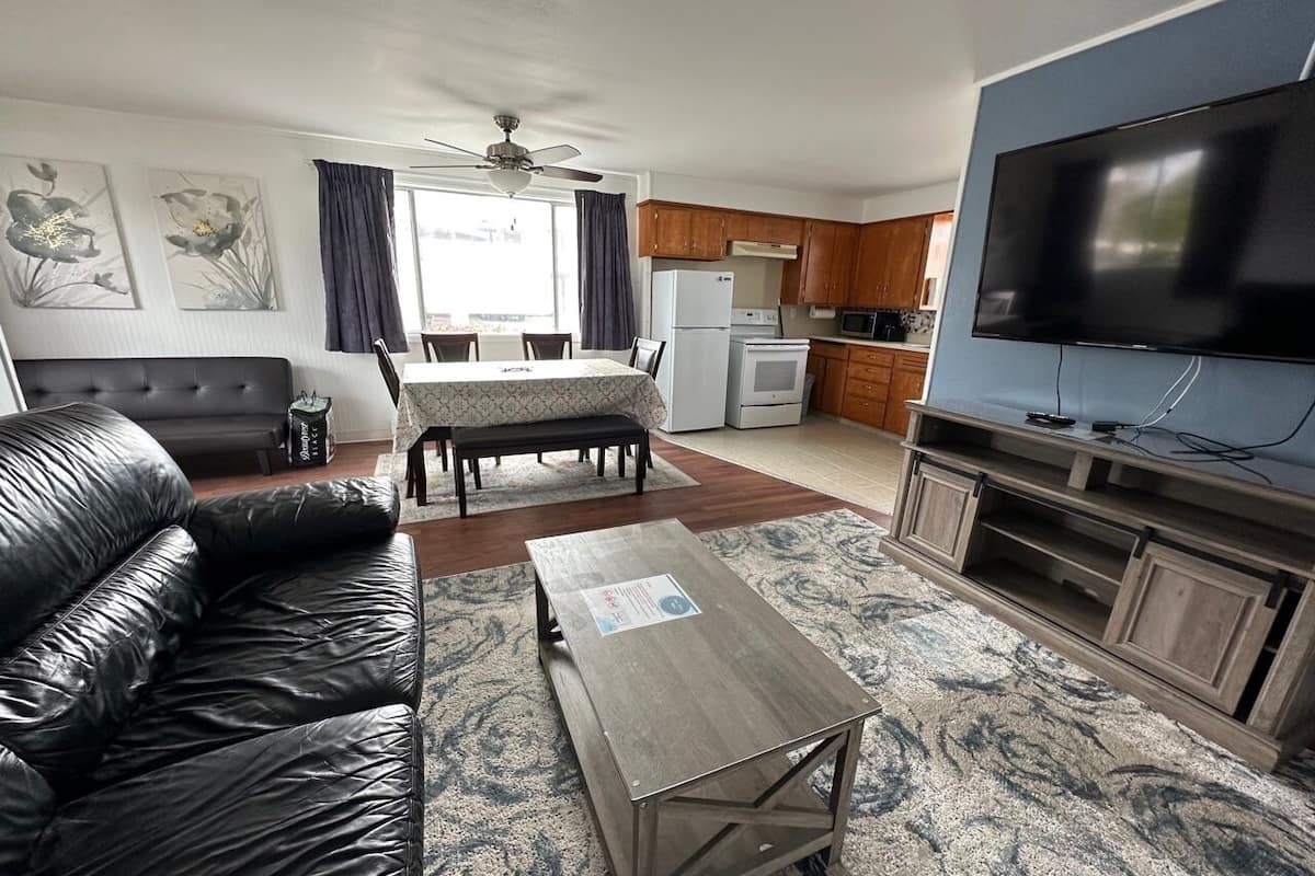 A living room with a leather sofa, a dining table, and a kitchen area with a TV.