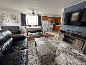 A living room with a leather sofa, a dining table, and a kitchen area with a TV. - Capt John's Motel (Coos Bay)
