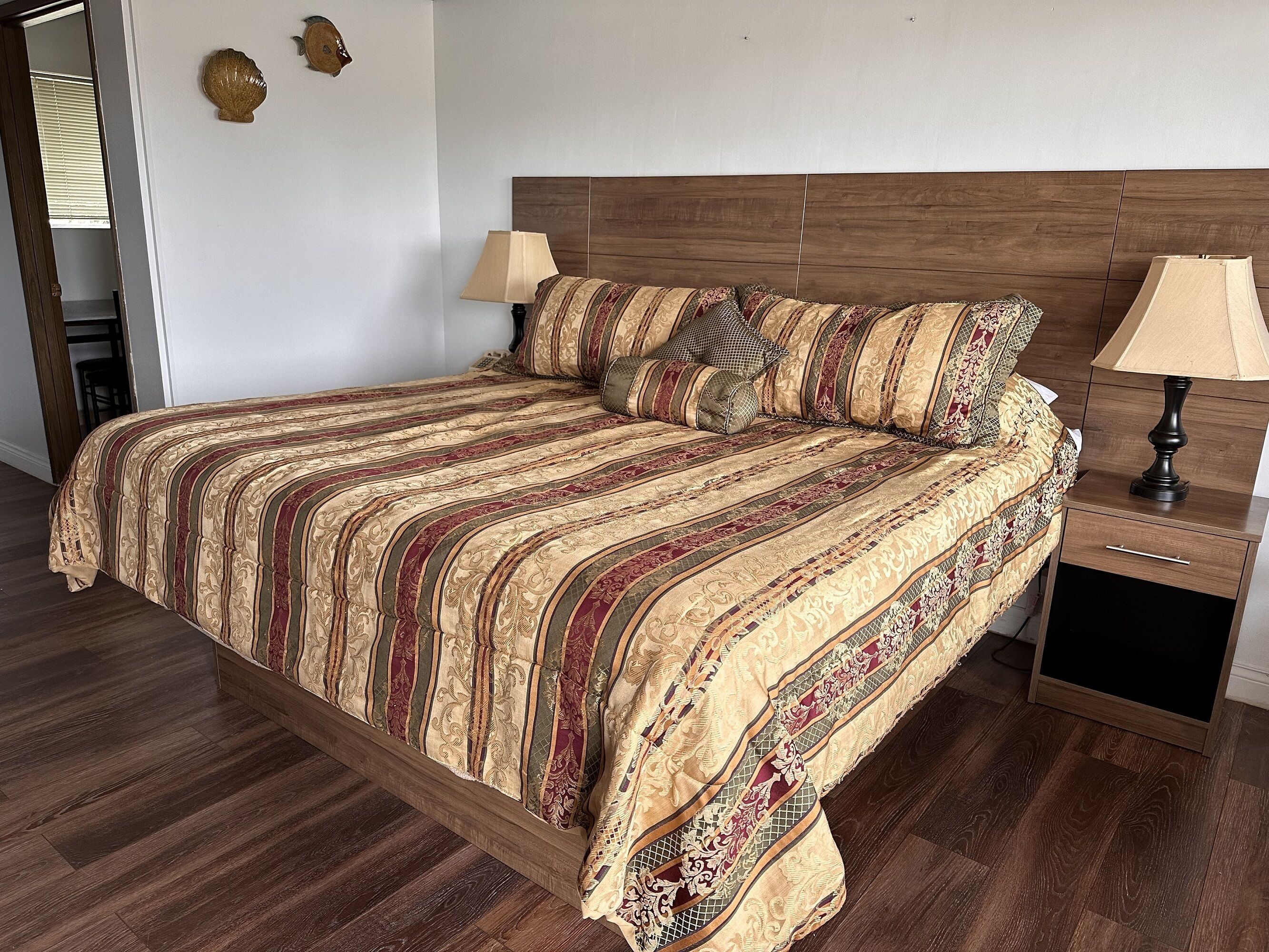 Quarto com cama de madeira, mesa de cabeceira, duas luminárias e espelho.