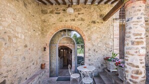 Un patio con pareti in pietra, un tavolo e sedie in ferro battuto, un arco d'ingresso e una pianta in vaso.