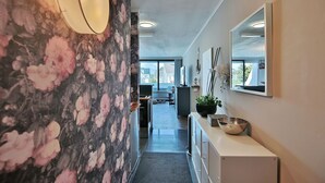A hallway with a floral wallpaper, a white radiator, a mirror, and a potted plant.
