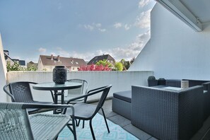 A balcony with outdoor furniture, a round table, and a view of houses and trees.