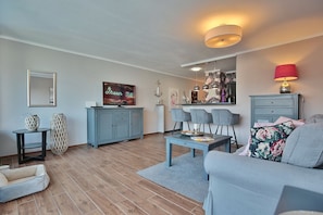 A modern living room with a grey sofa, a coffee table, and a TV on a stand. There is a blue cabinet and a small table with decorative items. - Haus Bergstraße 35 - Ferienhaus Bergstraße 35 Appartement 16 (Timmendorfer Strand)