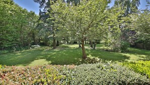 Un jardín bien cuidado con diversos árboles y arbustos, cielo despejado y césped impecable.