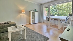 Una sala de estar moderna con un sofá, una mesa de centro, una lámpara, un aparador y un comedor con sillas y una mesa.