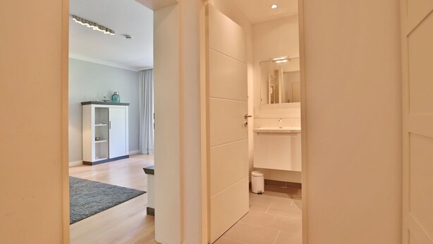 Un pasillo moderno con suelo de madera, un armario blanco y un pequeño cubo de basura.