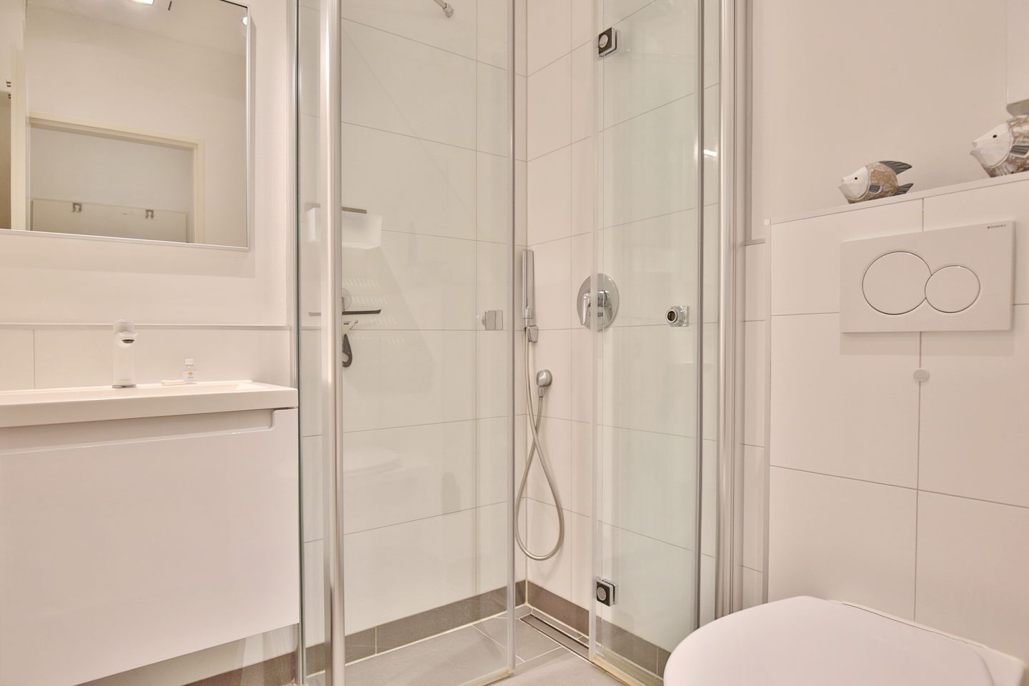 A modern bathroom with a glass shower enclosure, a toilet, and a sink with a mirror above.