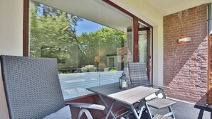 Un área de estar moderna al aire libre con una puerta de cristal que da a un patio, una pared de ladrillo y una mesa y sillas de metal.
