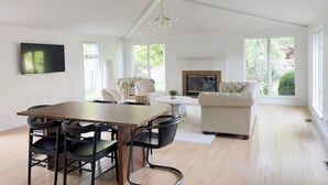Amplia sala de estar con chimenea, zona de comedor con mesa y sillas, y ventanas grandes que ofrecen vistas al exterior.