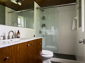 Een moderne badkamer met een houten wastafelmeubel, een glazen douchecabine en een wit toilet.