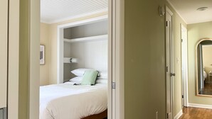 Un dormitorio con cama, mesita de noche, espejo y puerta que da a otra habitación.