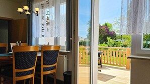 Un comedor con dos sillas de madera y una mesa, una araña y vistas a una terraza de madera y un jardín a través de una puerta de cristal.