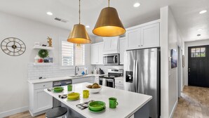 Une cuisine moderne avec des meubles blancs, des appareils en acier inoxydable et un îlot central doté de tabourets.