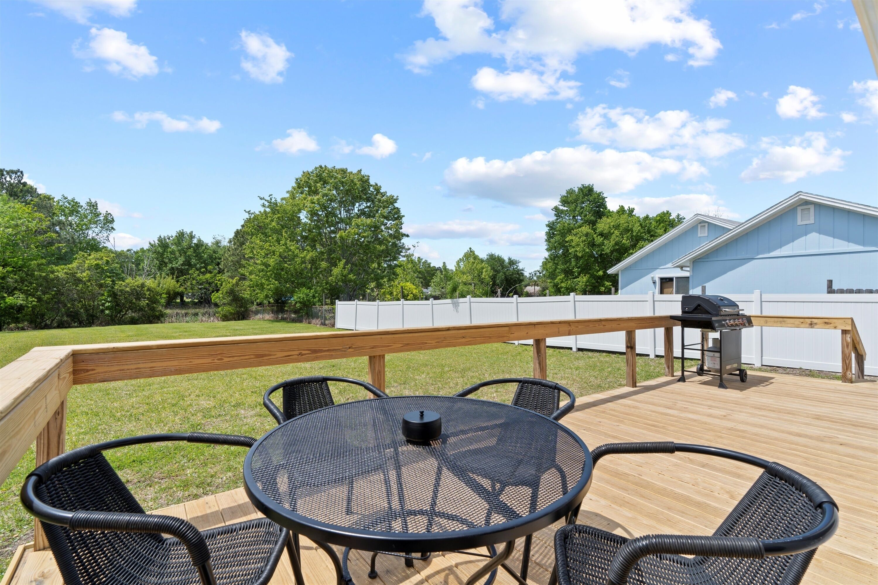 A wooden deck with a round table and chairs, a barbecue grill, and a white fence.