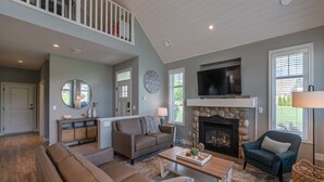 A spacious living room with a fireplace, a television mounted above it, and a comfortable seating area with sofas and a coffee table. - The Lakehouse/Snow Vacation Rental (Osoyoos)