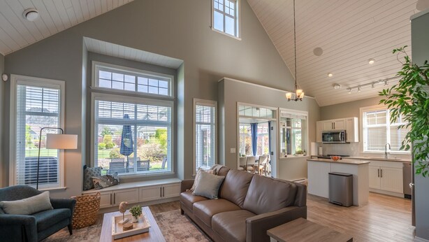A spacious living room with a large brown leather sofa, a coffee table, and a dining area with a table and chairs. There is a kitchen with white cabinets and a sink. - The Lakehouse/Snow Vacation Rental (Osoyoos)