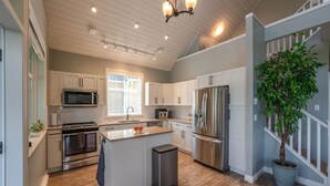 A modern kitchen with white cabinets, stainless steel appliances, a central island, and a potted plant. - The Lakehouse/Snow Vacation Rental (Osoyoos)