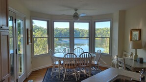 A dining area with a view of a lake, a ceiling fan, and a table with chairs. - Private Beach on Pond, Linens Included, Kayak & Canoe. All Rooms w/ Pond Views! (Chatham)