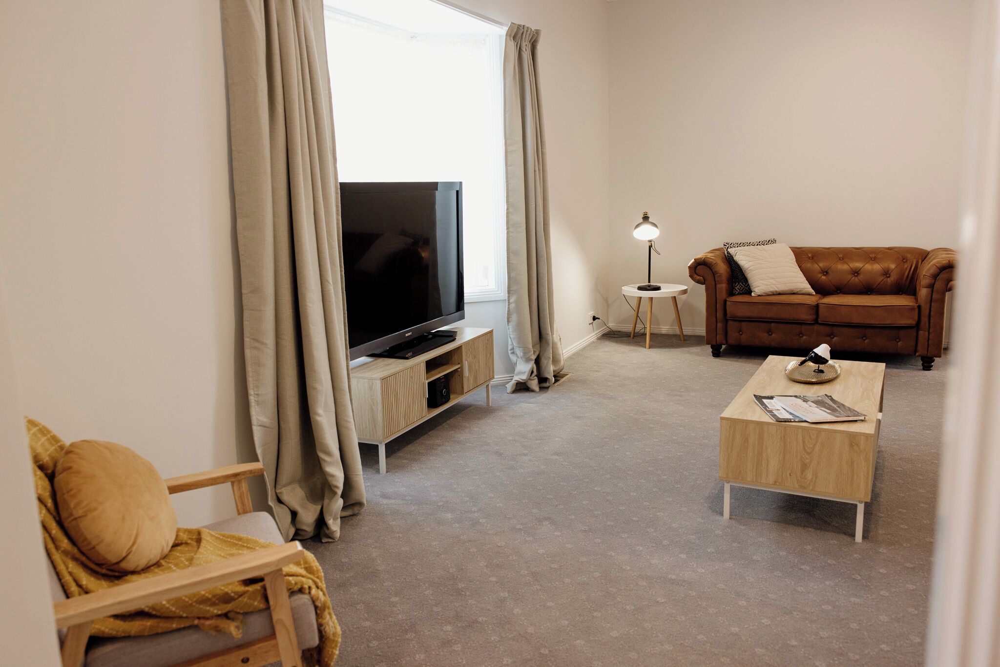 Ein Wohnzimmer mit Fernseher, einem braunen Sofa, einem Holztisch und einem kleinen Beistelltisch mit Lampe.