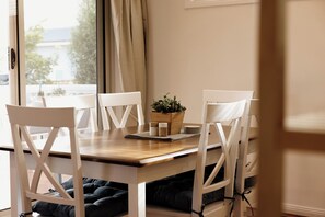 A dining area with a wooden table, white chairs, a plant centerpiece, and a view through a window. - Family, Pet  & EV Friendly Home in Bowral Centre (Bowral)