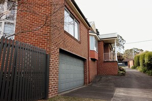 A two-story brick house with a grey garage door, a balcony, and a fenced driveway. - Family, Pet  & EV Friendly Home in Bowral Centre (Bowral)