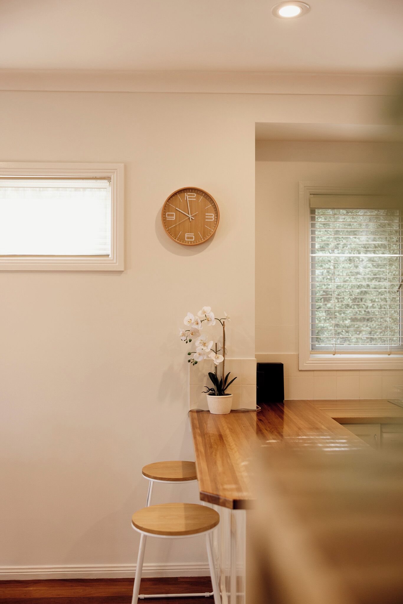 A kitchen with a wooden countertop, a clock, and a window with blinds.