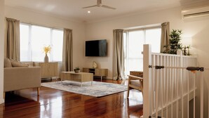A spacious living room with a wooden floor, a ceiling fan, a flat-screen TV, and a white gate. - Family, Pet  & EV Friendly Home in Bowral Centre (Bowral)