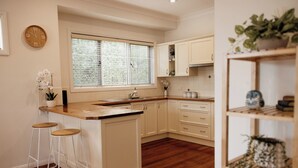 A kitchen with wooden flooring, white cabinets, a window with blinds, and a clock on the wall. - Family, Pet  & EV Friendly Home in Bowral Centre (Bowral)