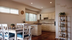 A modern kitchen with white cabinets, a wooden dining table with blue cushions, and a built-in island. - Family, Pet  & EV Friendly Home in Bowral Centre (Bowral)