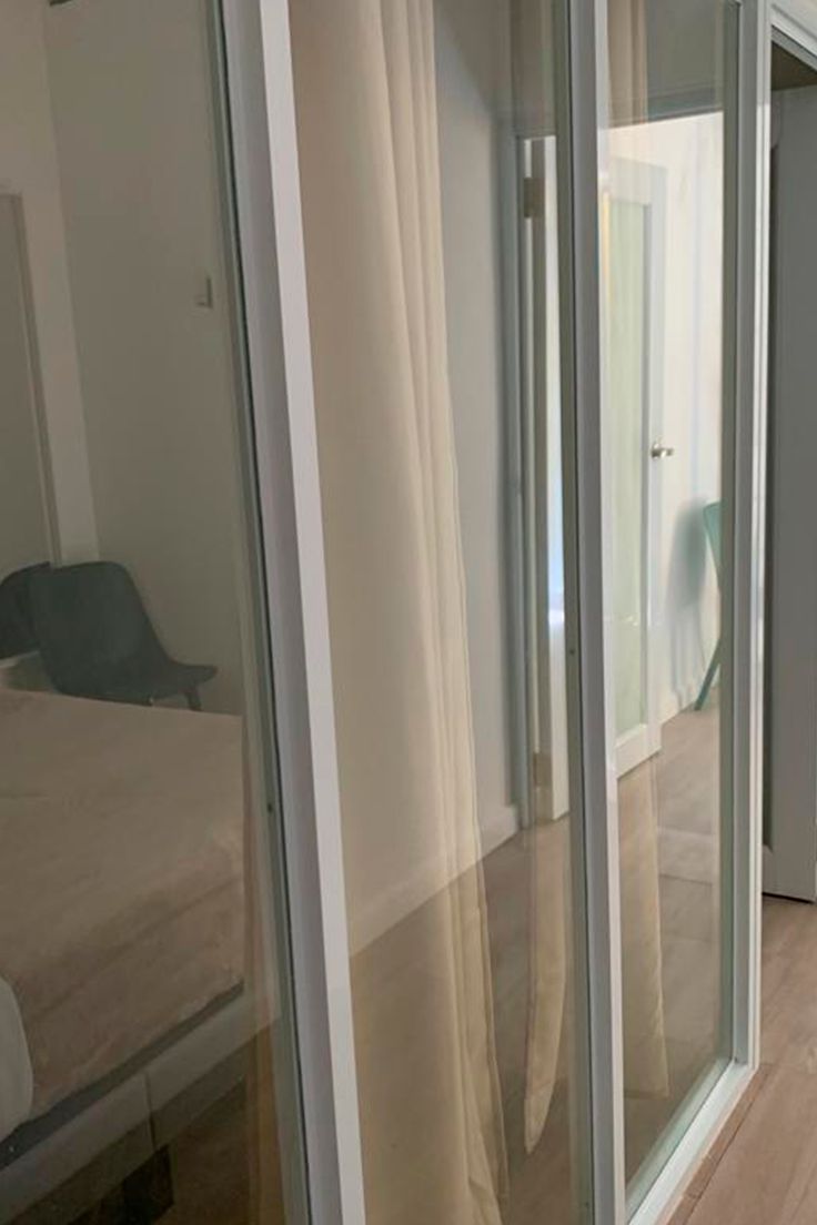 Una habitación con una cama, una silla y un ventanal de vidrio que da a otra estancia.