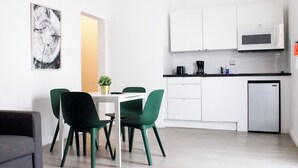 Eine moderne Küche mit weißen Schränken, einer Mikrowelle und einer Kaffeemaschine. Es gibt einen Essbereich mit einem Tisch und vier Stühlen.