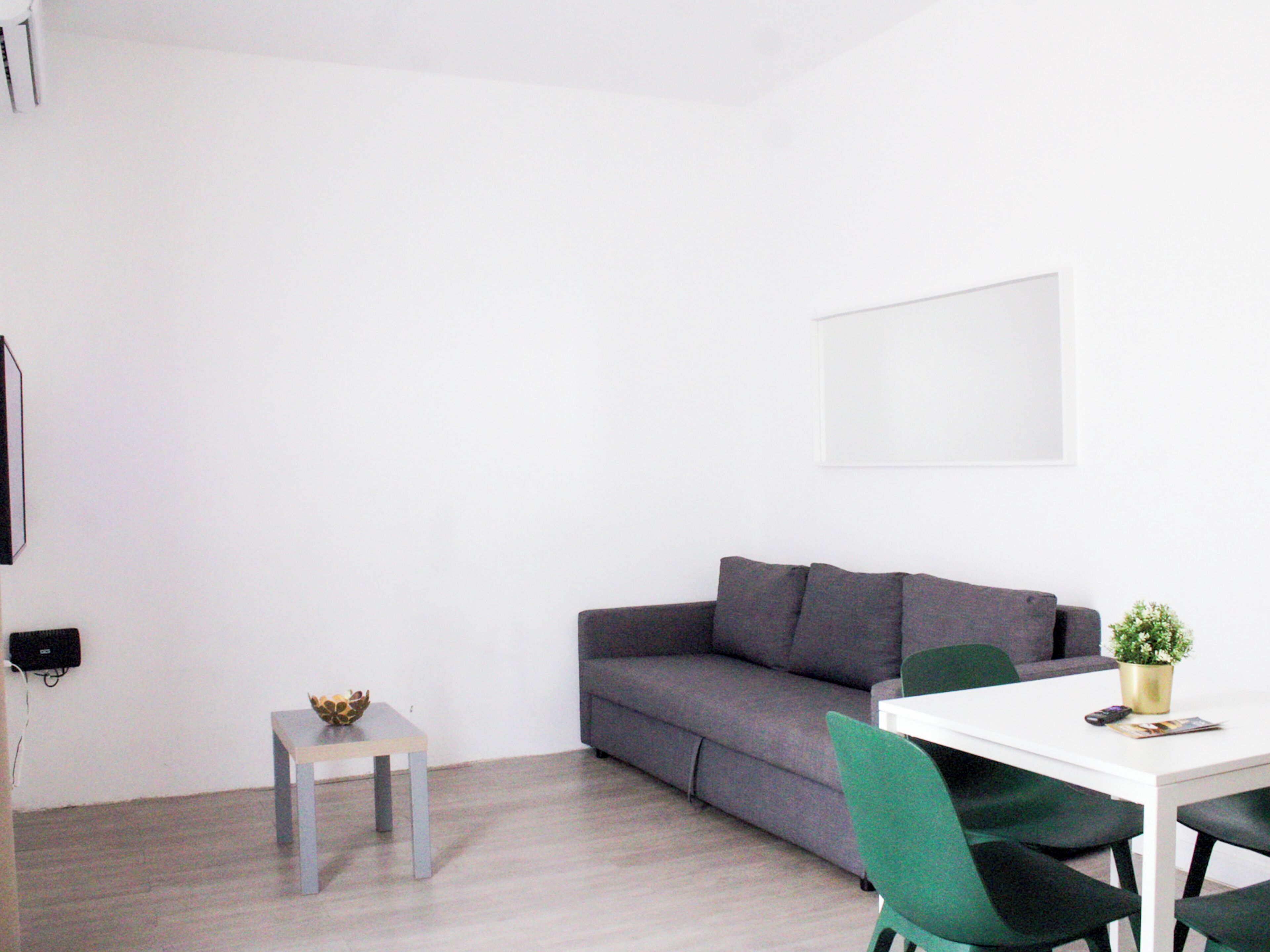 A modern living room with a grey sofa, a small side table, a white coffee table, and green chairs.