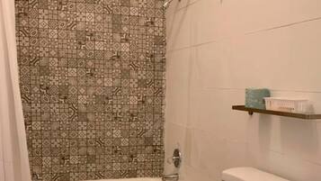 Un baño con ducha, inodoro y un estante pequeño con artículos de tocador.