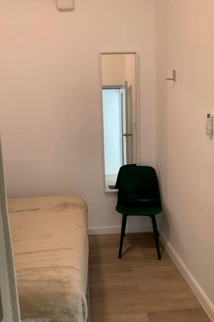 A small room with a bed, a chair, a mirror, and a window.