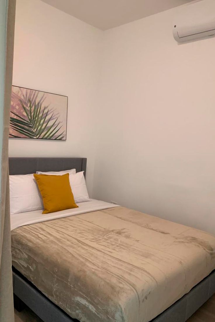 A single bed with a headboard, a single yellow pillow, and a wall-mounted air conditioner.