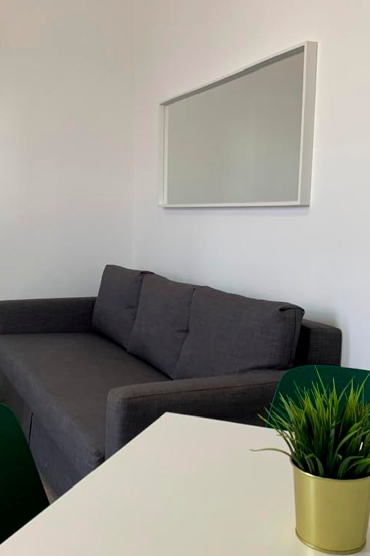 A modern living room with a grey sofa, a white table, and a green plant in a gold pot.