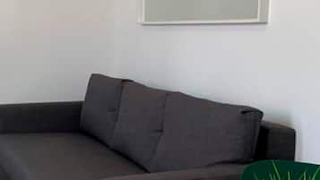 A modern living room with a grey sofa, a white table, and a green plant in a gold pot.