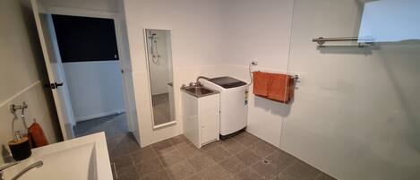 A compact bathroom with a shower, a sink, and a washing machine.