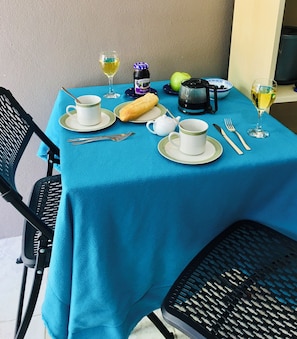Une table dressée pour le petit-déjeuner, avec une nappe bleue, une cafetière, un pot de confiture aux myrtilles de la marque Smuckers, une miche de pain et deux verres à vin.