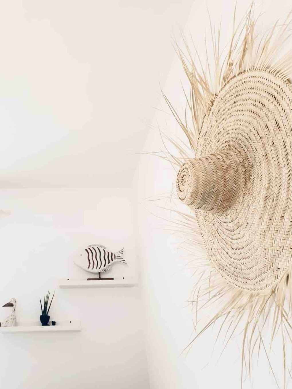 Una habitación con pared blanca, lámpara colgante de fibras naturales, repisa con decoración de un pez pequeño y planta en maceta.