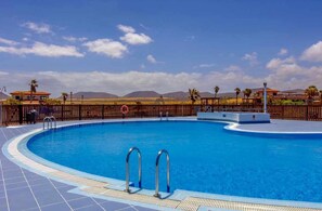 Una piscina con cerco de madera, palmeras y montañas al fondo.