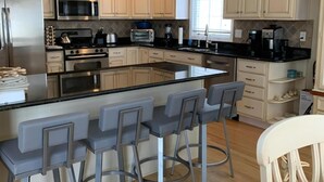A modern kitchen with white cabinets, stainless steel appliances, and a central island with bar stools. - One off with Views! Long Beach Twsp. (Brant Beach)