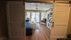 A spacious living room with a large sliding door leading to a balcony, a blue sofa, and a white cabinet with shelves. - One off with Views! Long Beach Twsp. (Brant Beach)