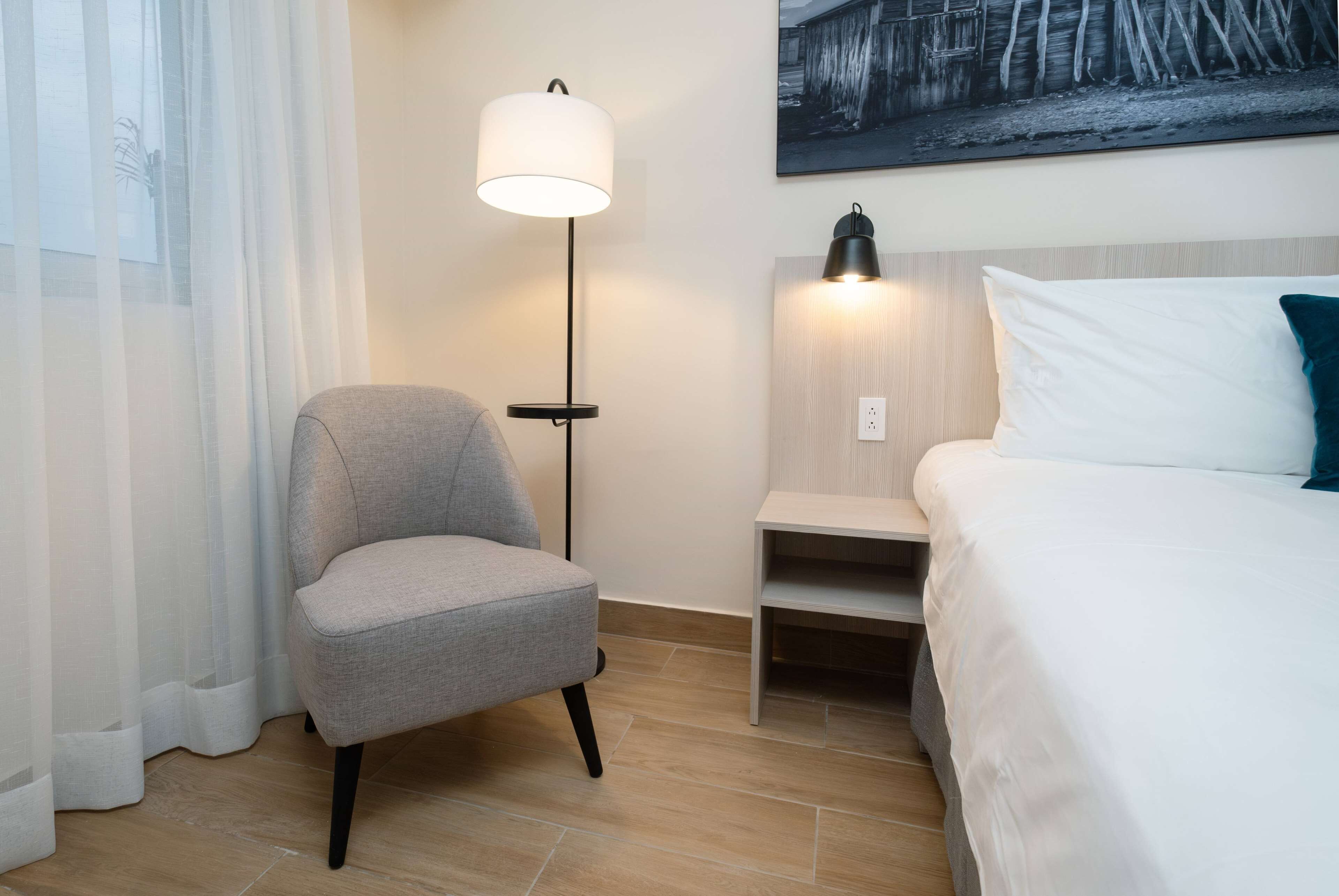Een hotelkamer met een bed, een stoel, een vloerlamp en een schilderij aan de muur.
